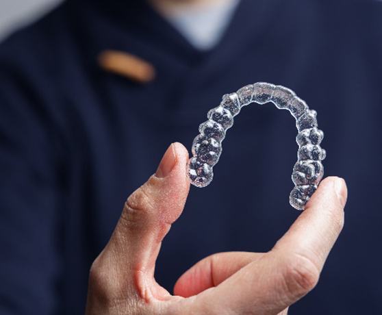Woman in grey shirt smiling while holding Invisalign