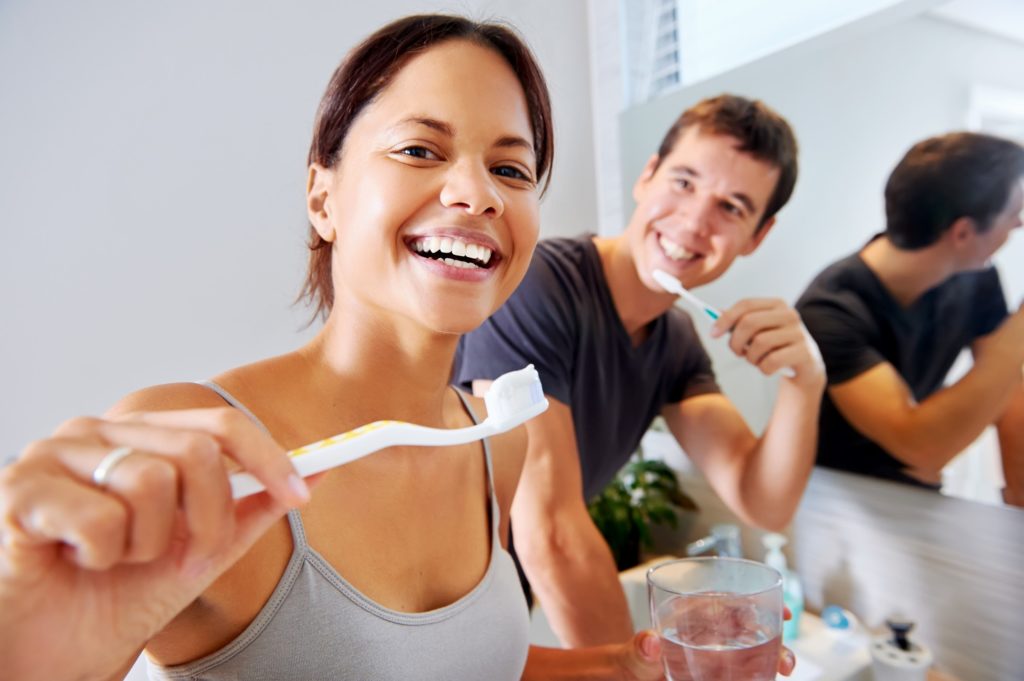 Happy couple smiling while brushing their teeth at home